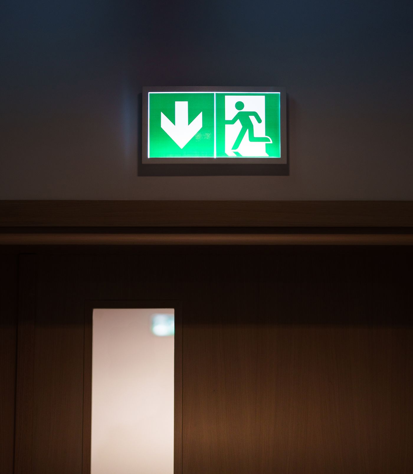 Placa verde iluminada indicando saída acima de uma porta